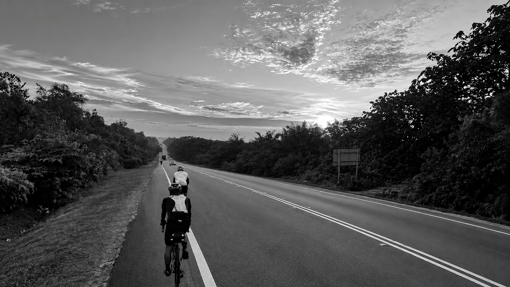 Randonneurs riding along a road at dawn in black and white